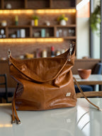 Tan brown, geniune leather slouchy handbag on a table with a blurred cafe interior in the background