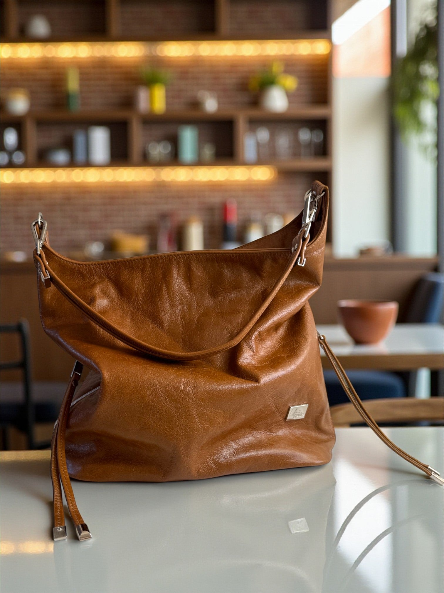 Tan brown, geniune leather slouchy handbag on a table with a blurred cafe interior in the background