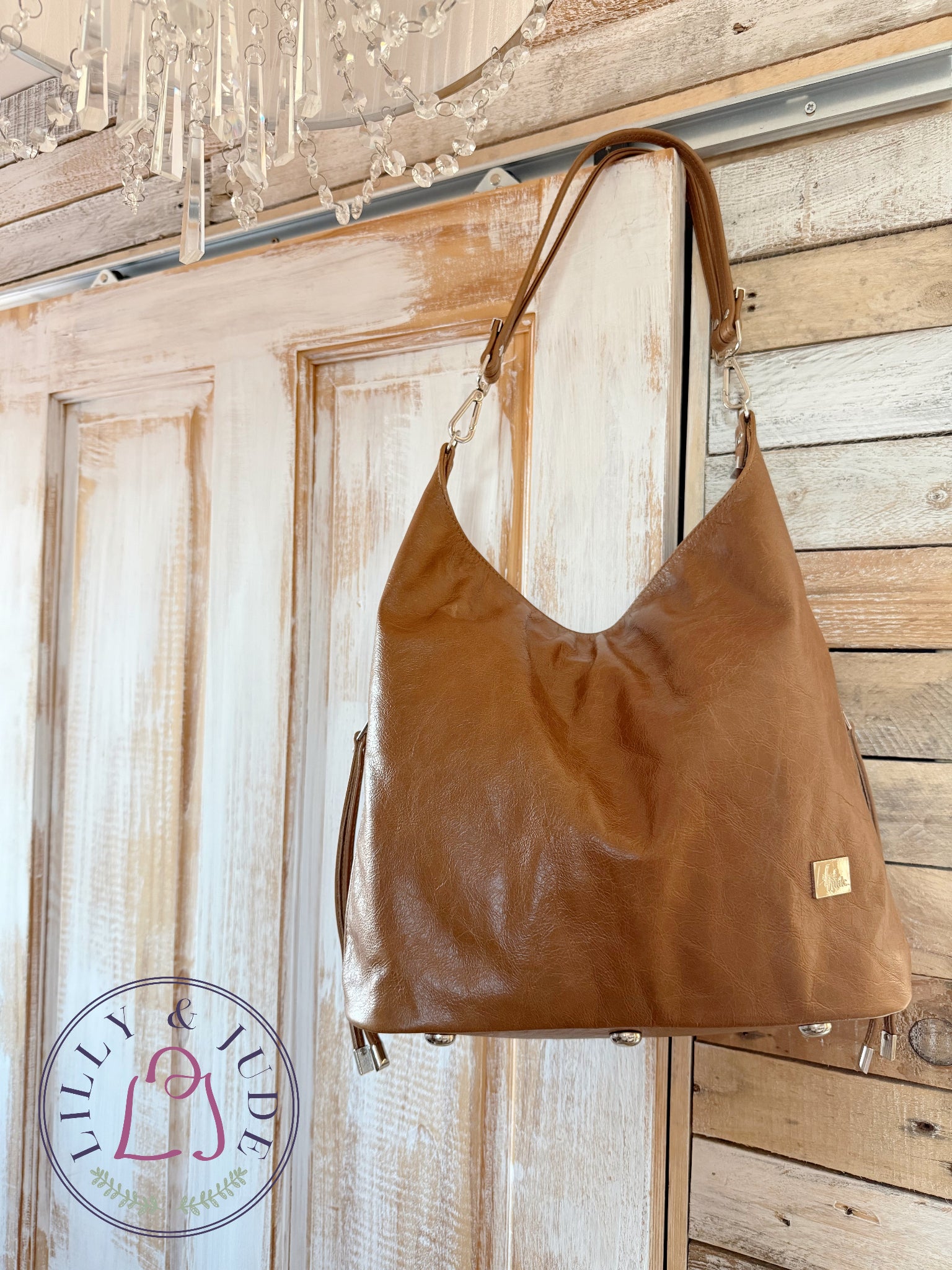 Brown, rescued  leather tote style handbag hanging on a wooden door with 'Lilly & Jude' logo tag.