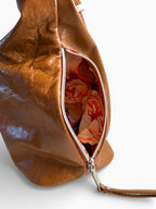 View of the unzipped side pocket of the tan leather, slouchy Simone handbag , showing the floral patterned interior lining on a white background