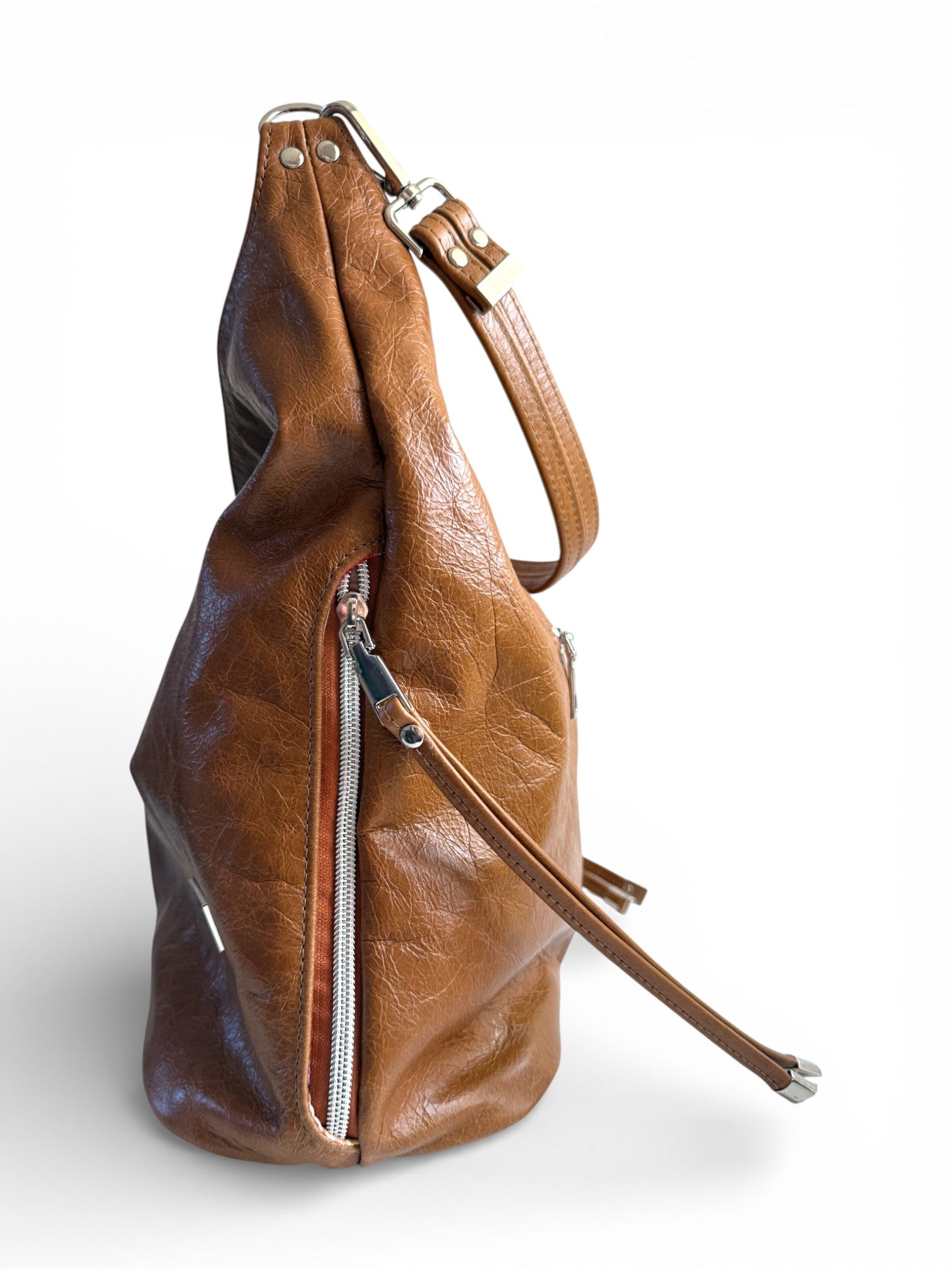 Side view of the brown, genuine  leather handbag with a shoulder strap and silver hardware, on a white background. The image highlights one of the side pockets, with a tassel attached to the zipper pull