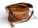 Tan brown leather slouch handbag with a strap on a white background