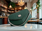 Forest green leather clutch handbag with a silver strap on a table in a restaurant setting