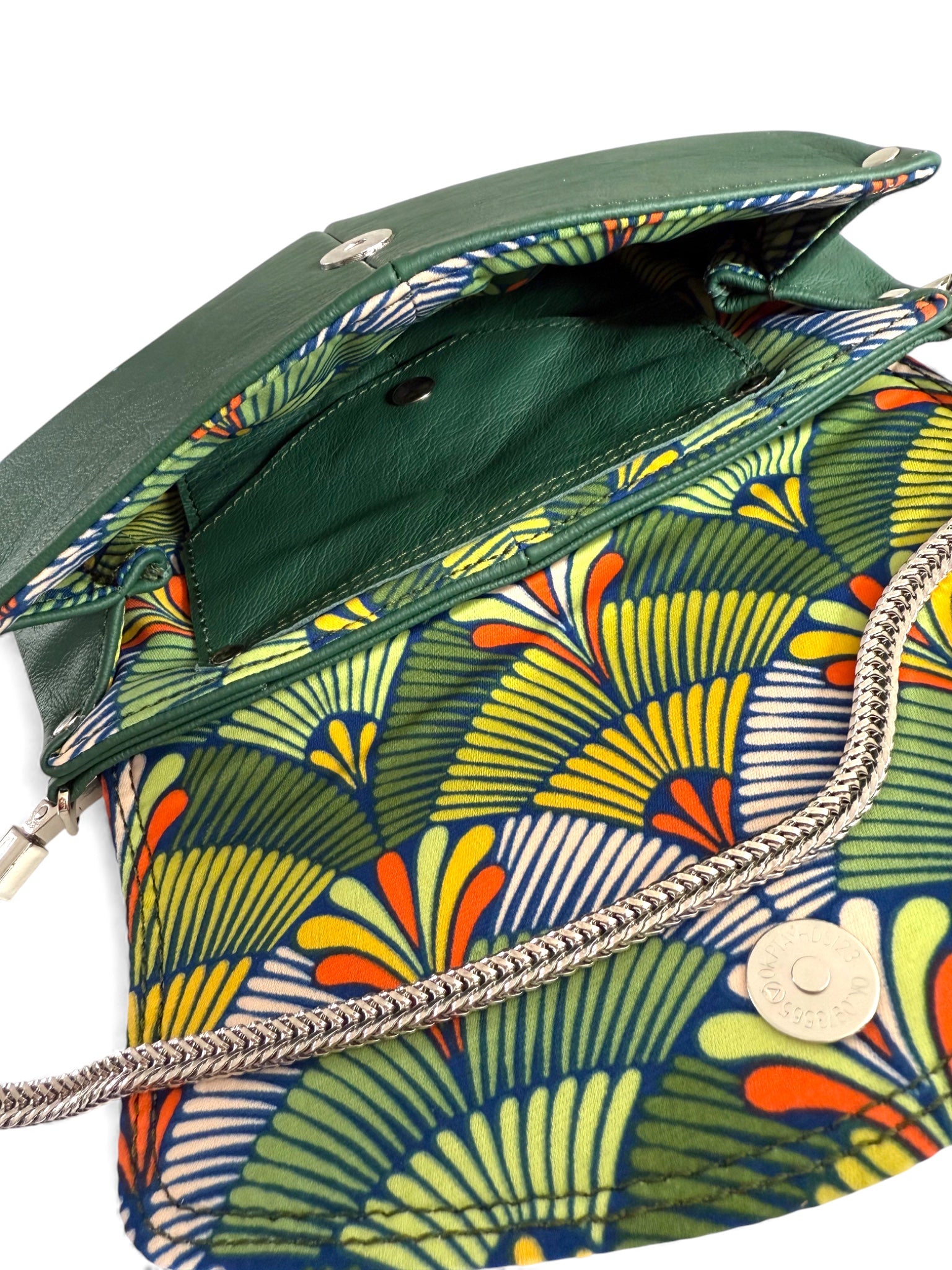 Interior view of a deep green handbag with colourful abstract patterned lining and chain detail on a white background. 