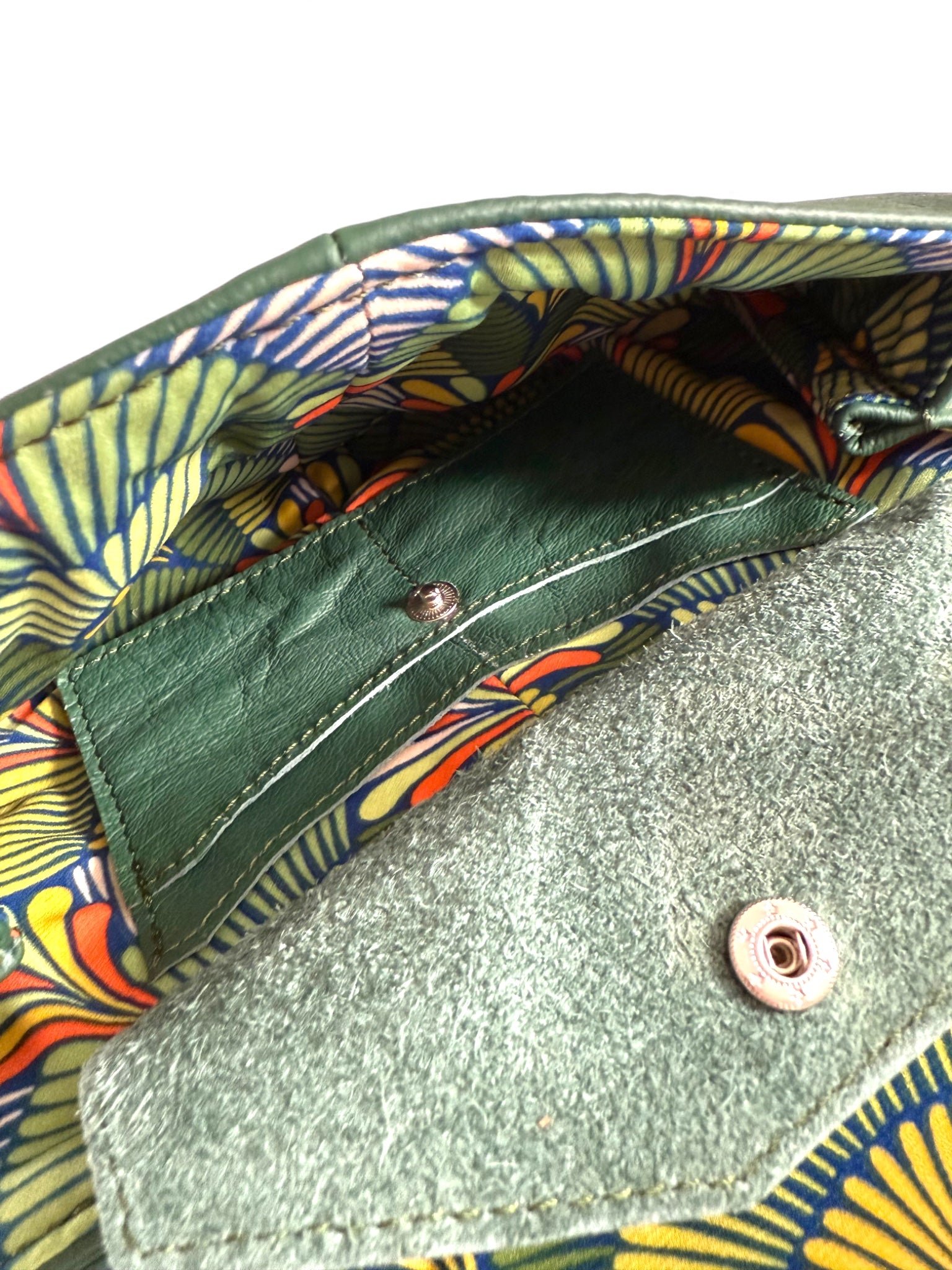 Close-up of the integrated purse with colourful fan patterned lining. The clutch is made from green leather 