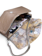 A tan leather clutch bag shown open, revealing a patterned interior with a silver chain strap, metal snap closure, and visible contents including cards and a lipstick