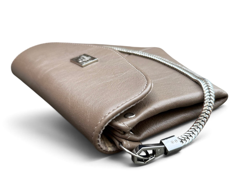 A side view of taupe leather clutch bag with a silver-tone chain strap and a small silver metal logo plaque, shown lying down on a white background.