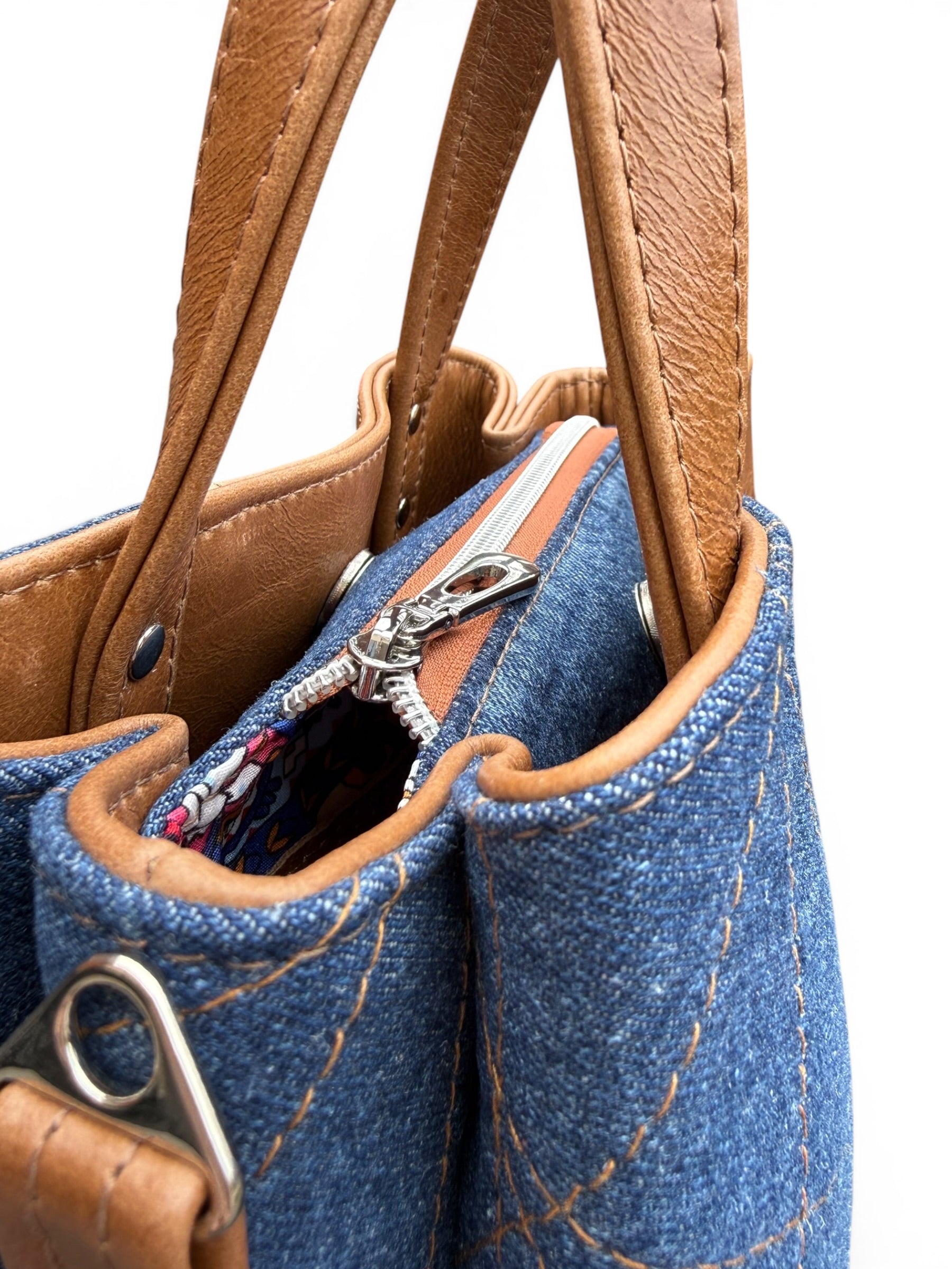 Close-up of a blue denim handbag with brown leather handles and trim.