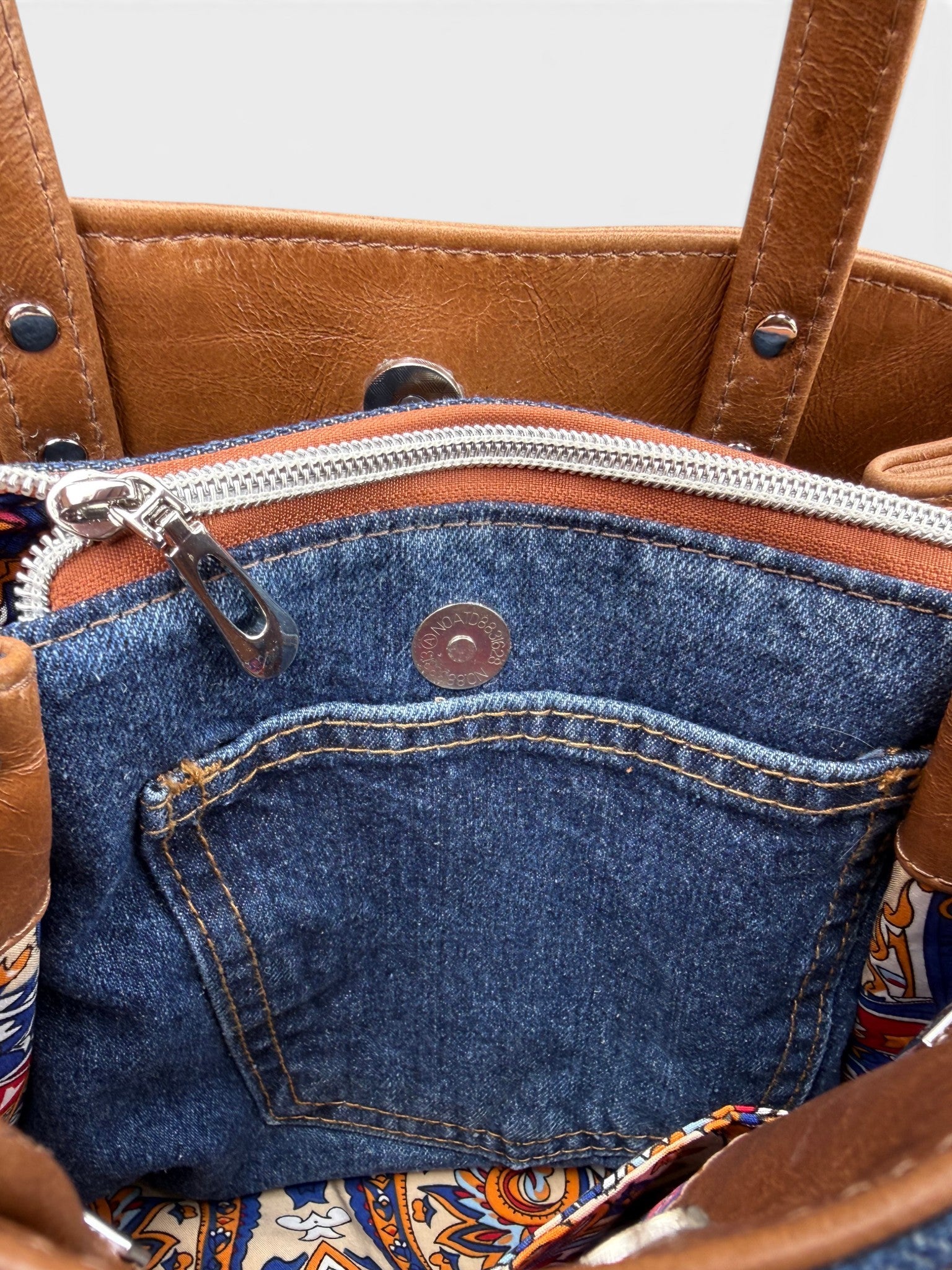 Close-up of a tan brown leather handbag with a blue denim pocket and colourful interior lining
