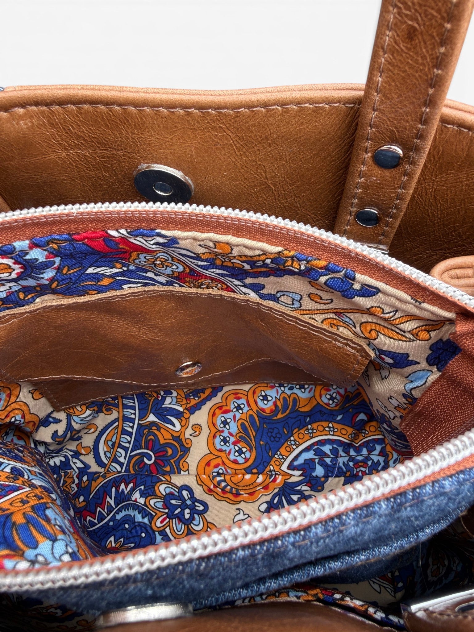 Close-up of a handbag with denim front pocket and patterned interior. The image shows the inside of the centre divider pocket, revealing the Lilly & Jude signature integrated purse