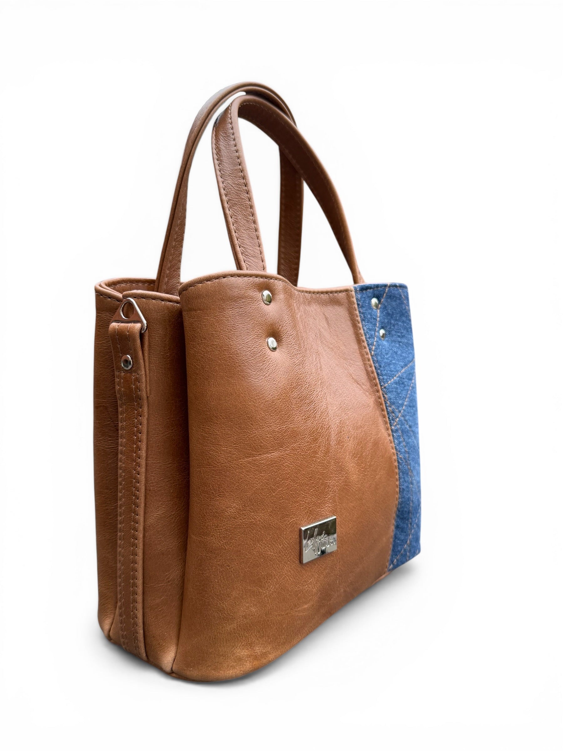 Front, side view of the Soraya tote style handbag, made from genuine, rescued tan Brown leather with a blue denim accent on a white background