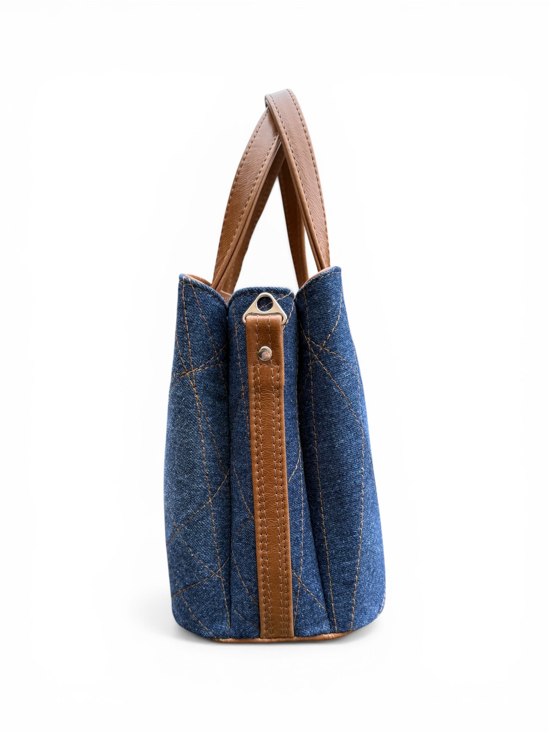 Side view of the Soraya bag, showing the blue denim side panel with brown leather strap holder and silver hardware on a white background