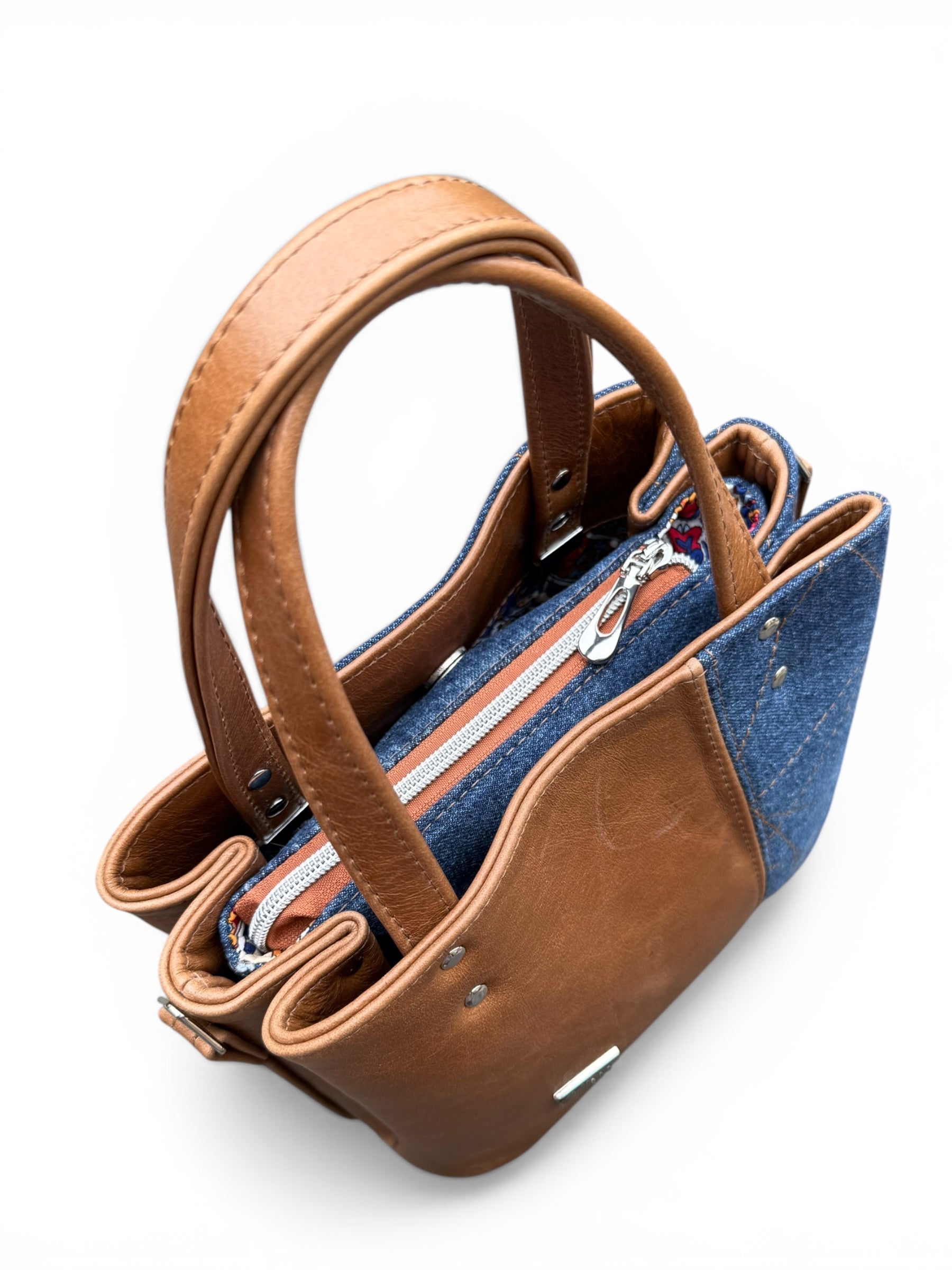 Birds eye view of the Soraya handbag which is made from tan coloured leather and upcycled denim, highlighting the denim zipper placket and closed silver zip
