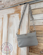 Gray genuine leather handbag with patterned strap hanging on a wooden door.