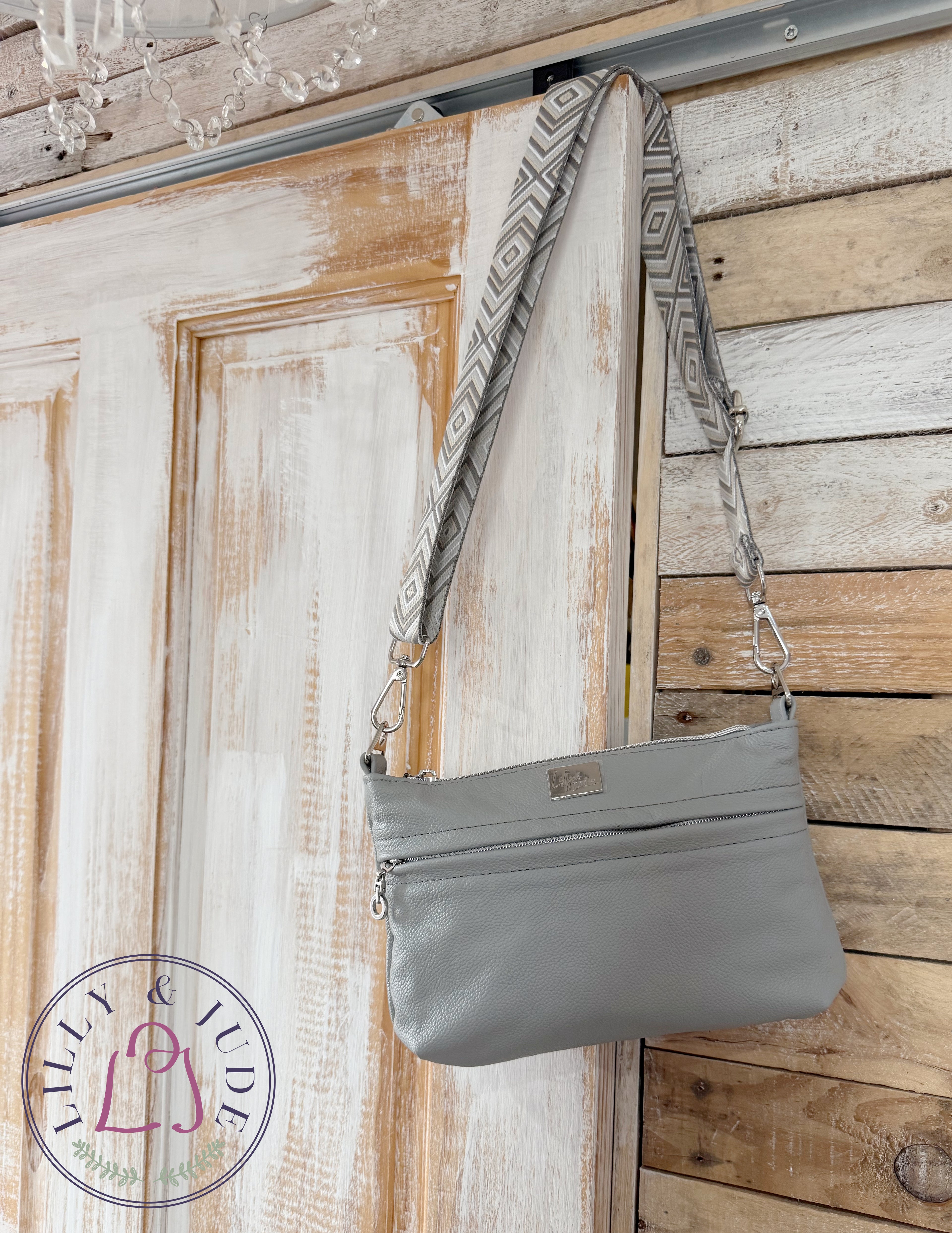 Gray genuine leather handbag with patterned strap hanging on a wooden door.