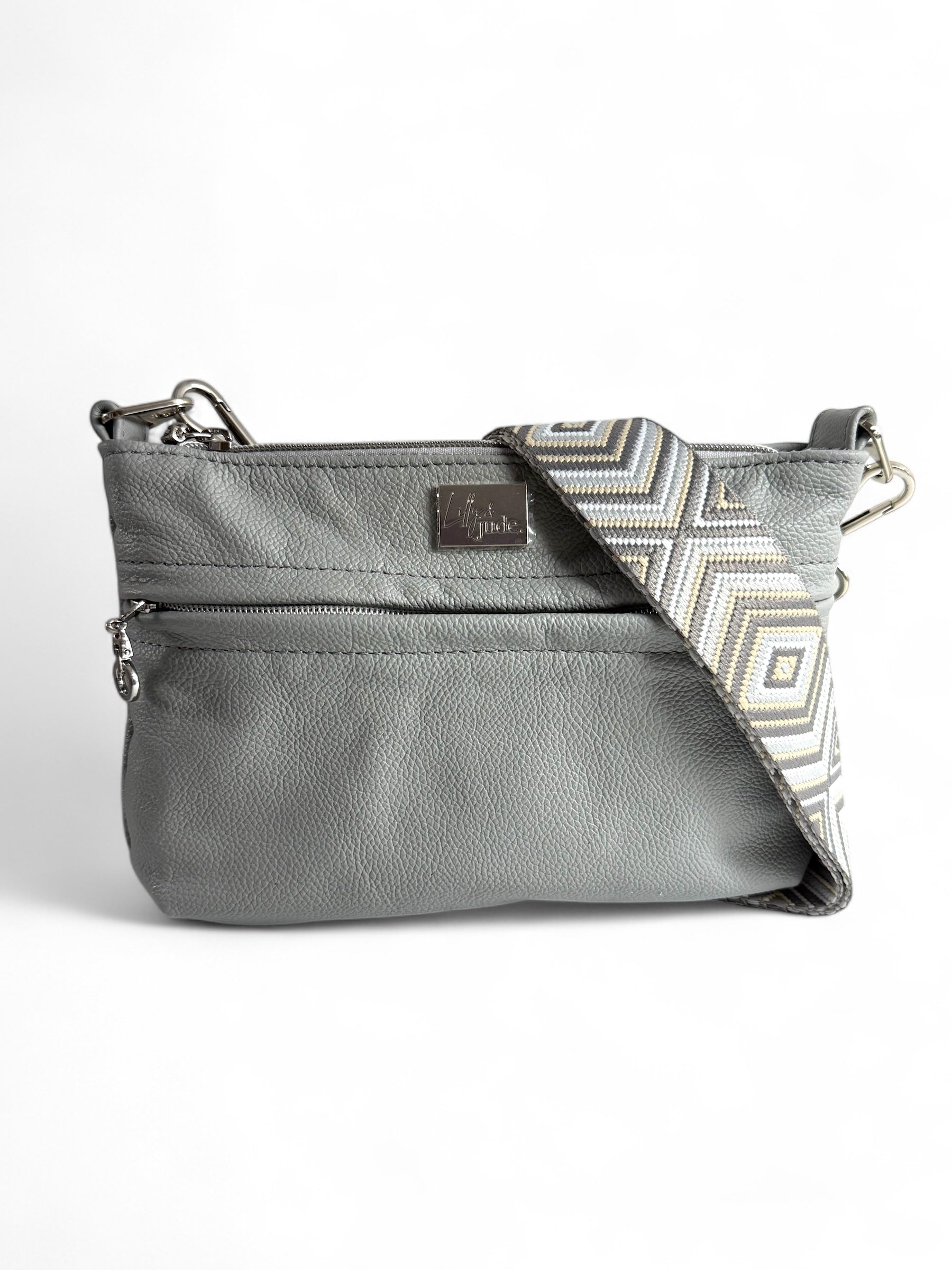 A light grey leather crossbody bag with a geometric pattern on the strap and silver hardware.