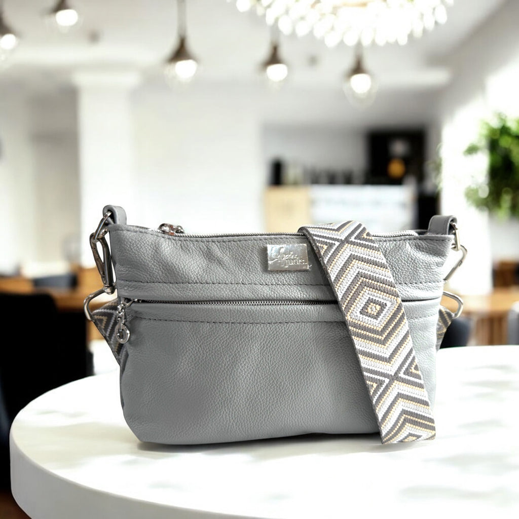 Gray handbag with a patterned strap on a white table in a blurred indoor background.