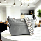 Gray handbag with a patterned strap on a white table in a blurred indoor background.