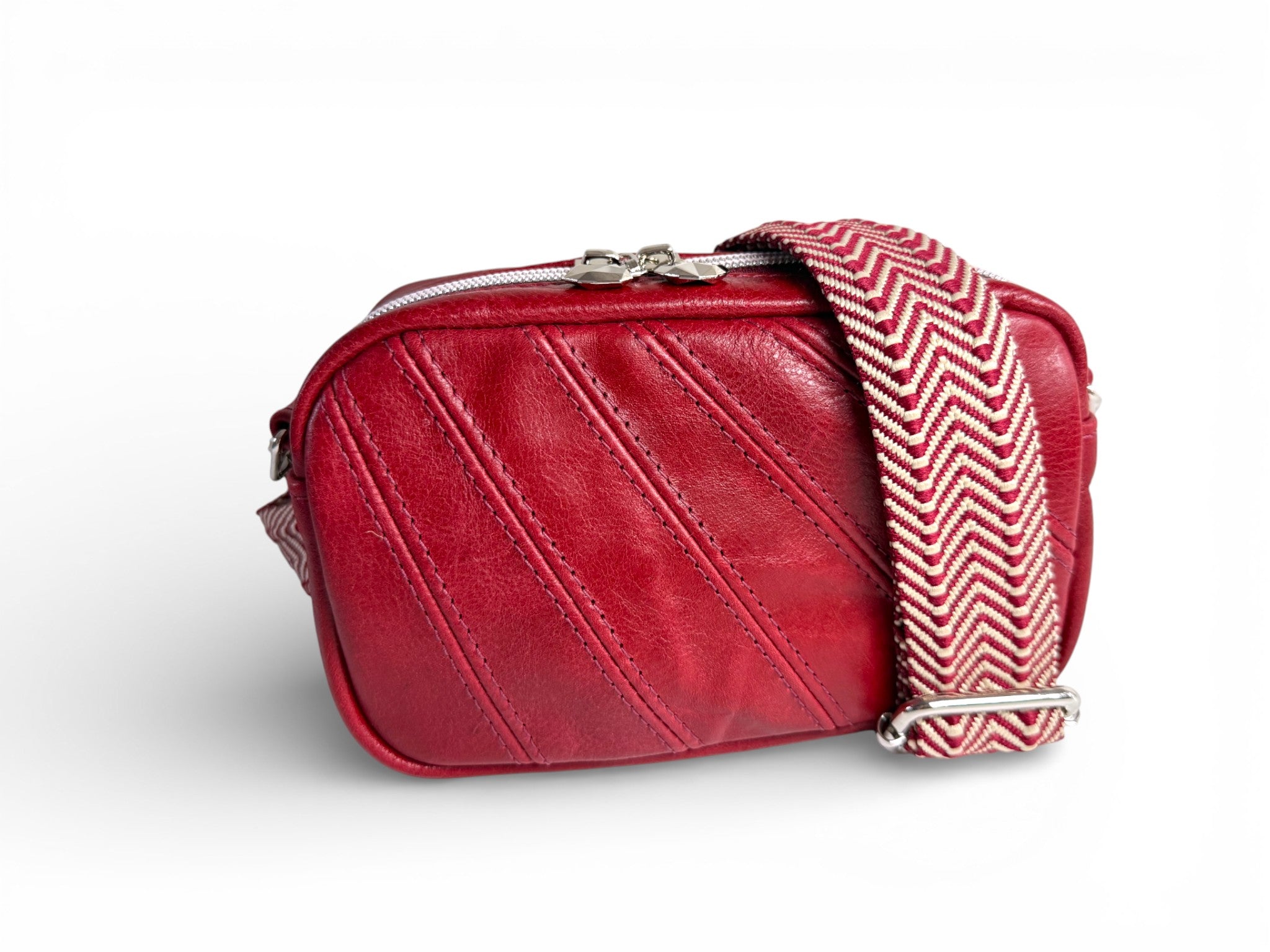 Small, red leather camera bag with a woven, removable, adjustable chevron patterned strap on a white background