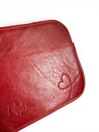 Close-up of a red leather bag, showing the stitched heart design, a 'Lilly & Jude' embossed logo, and the texture of the rescued leather, on a white background