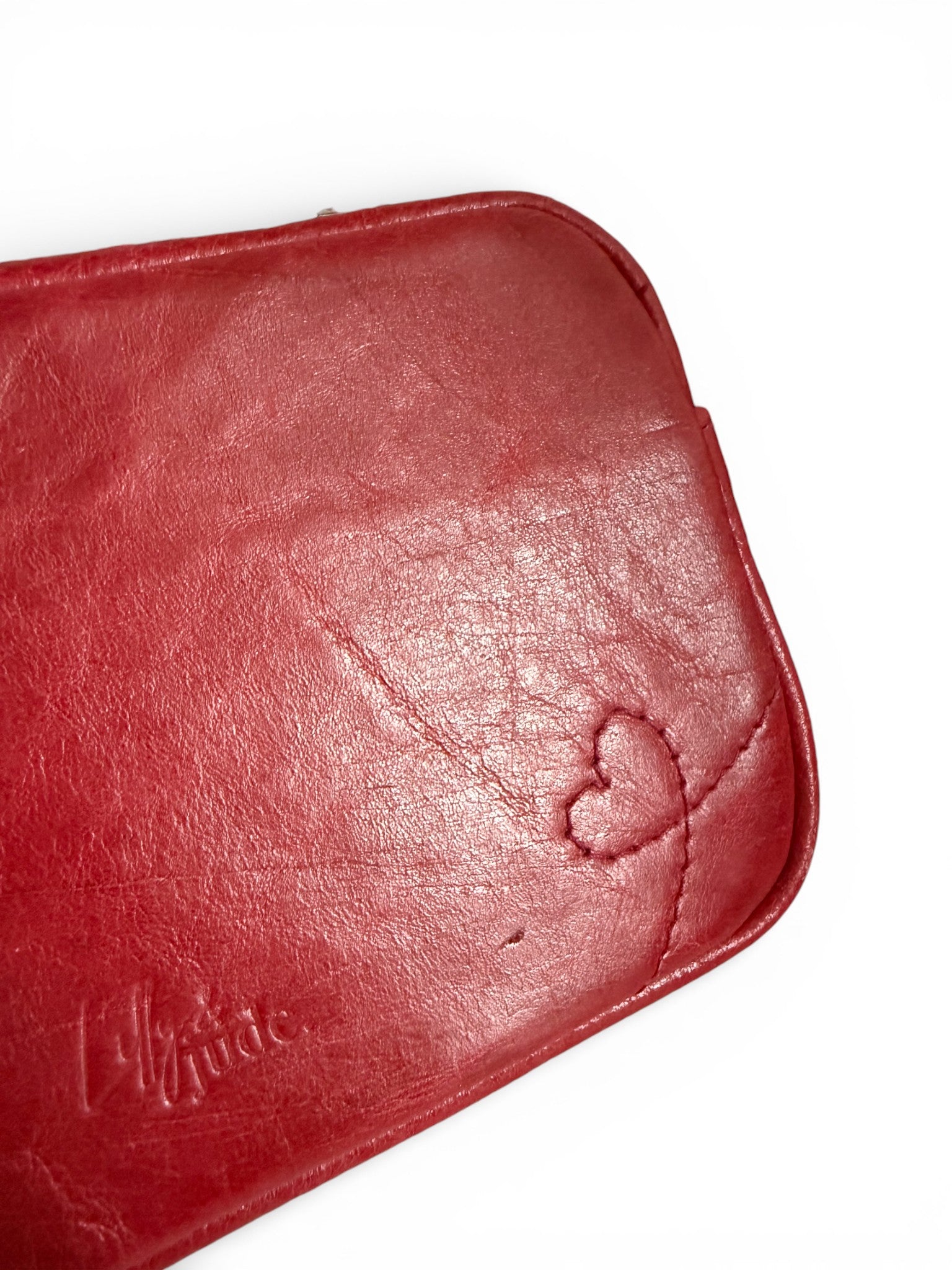 Close-up of a red leather bag, showing the stitched heart design, a 'Lilly & Jude' embossed logo, and the texture of the rescued leather, on a white background