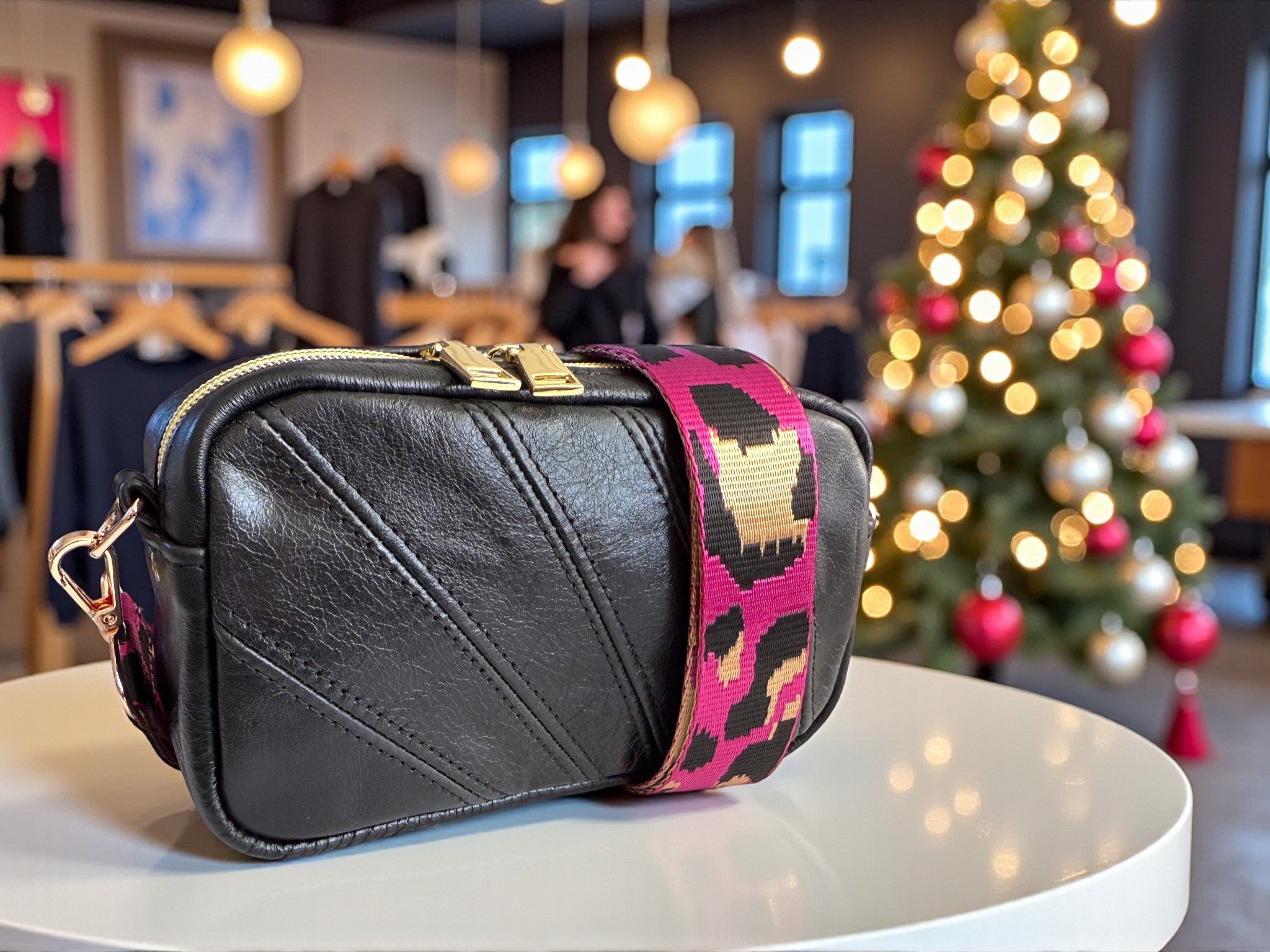 Black leather crossbody bag with a colourful strap on a table in a room with a Christmas tree.