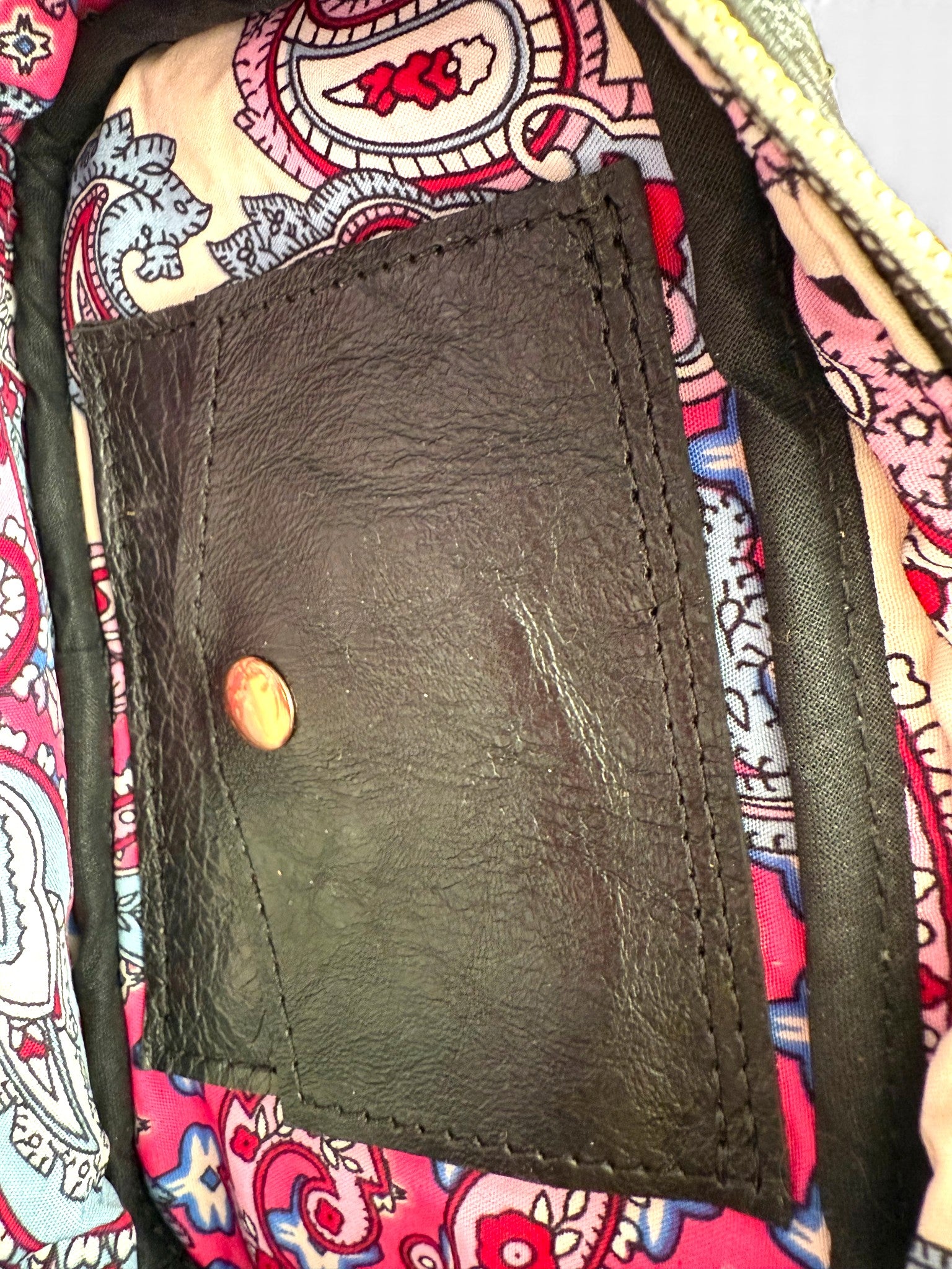 Close-up of a brown leather cardholder with a press stud on a colorful patterned fabric background