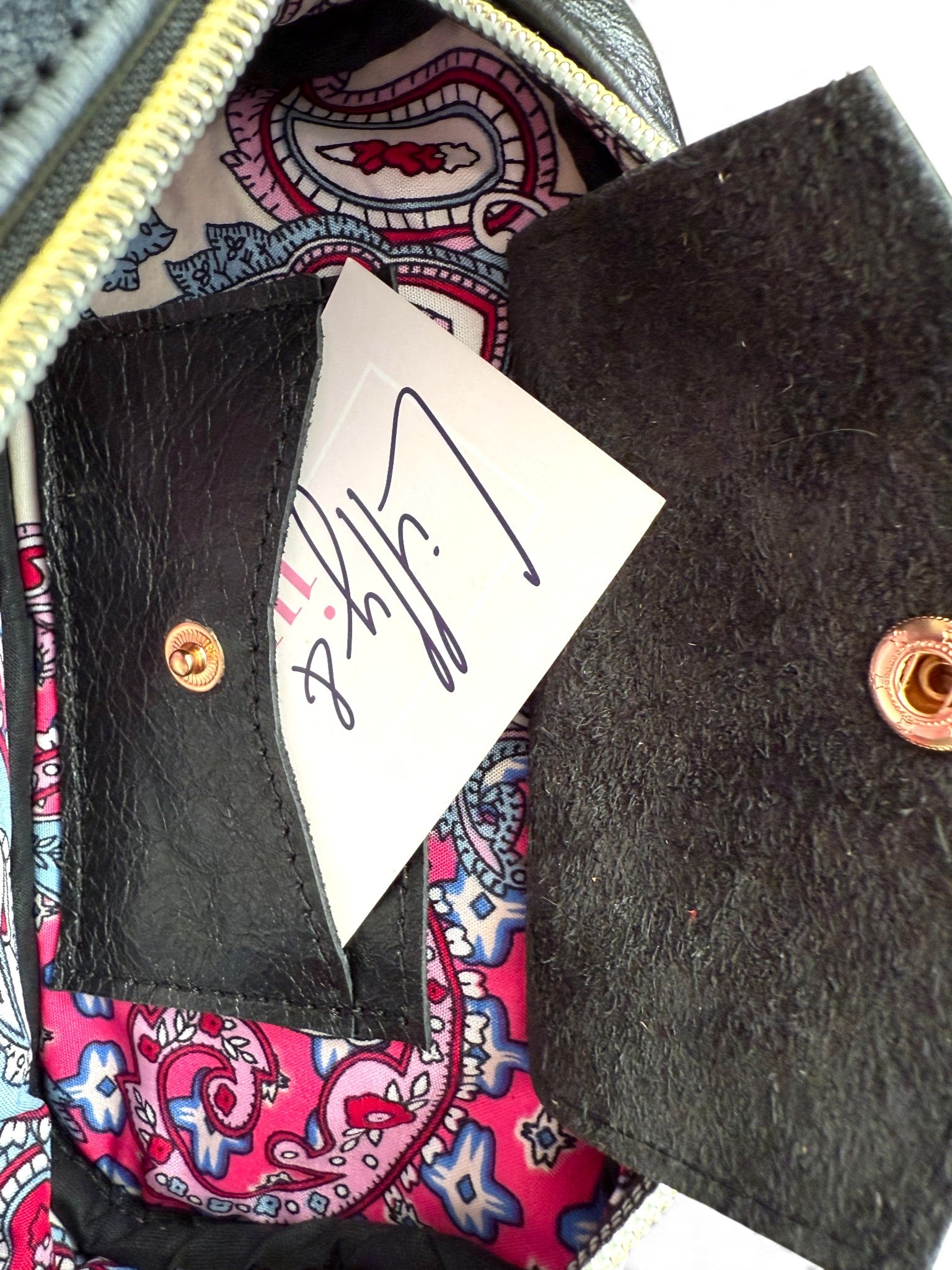 Close-up of a black leather wallet with a pink and blue paisley patterned interior, featuring a brand card.