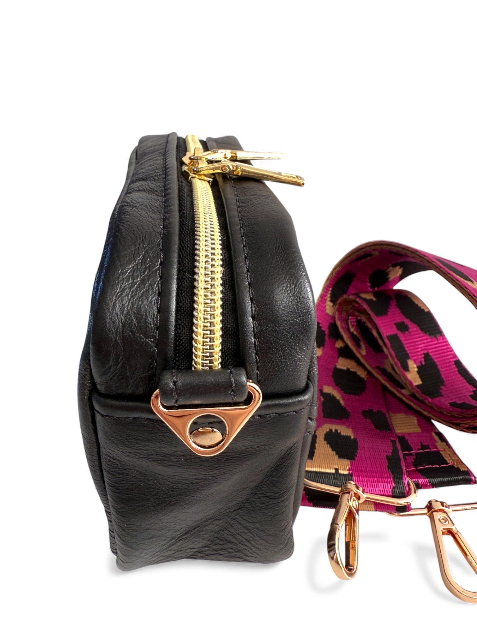 Black leather crossbody bag with gold zipper and fuschia pink leopard print strap on a white background