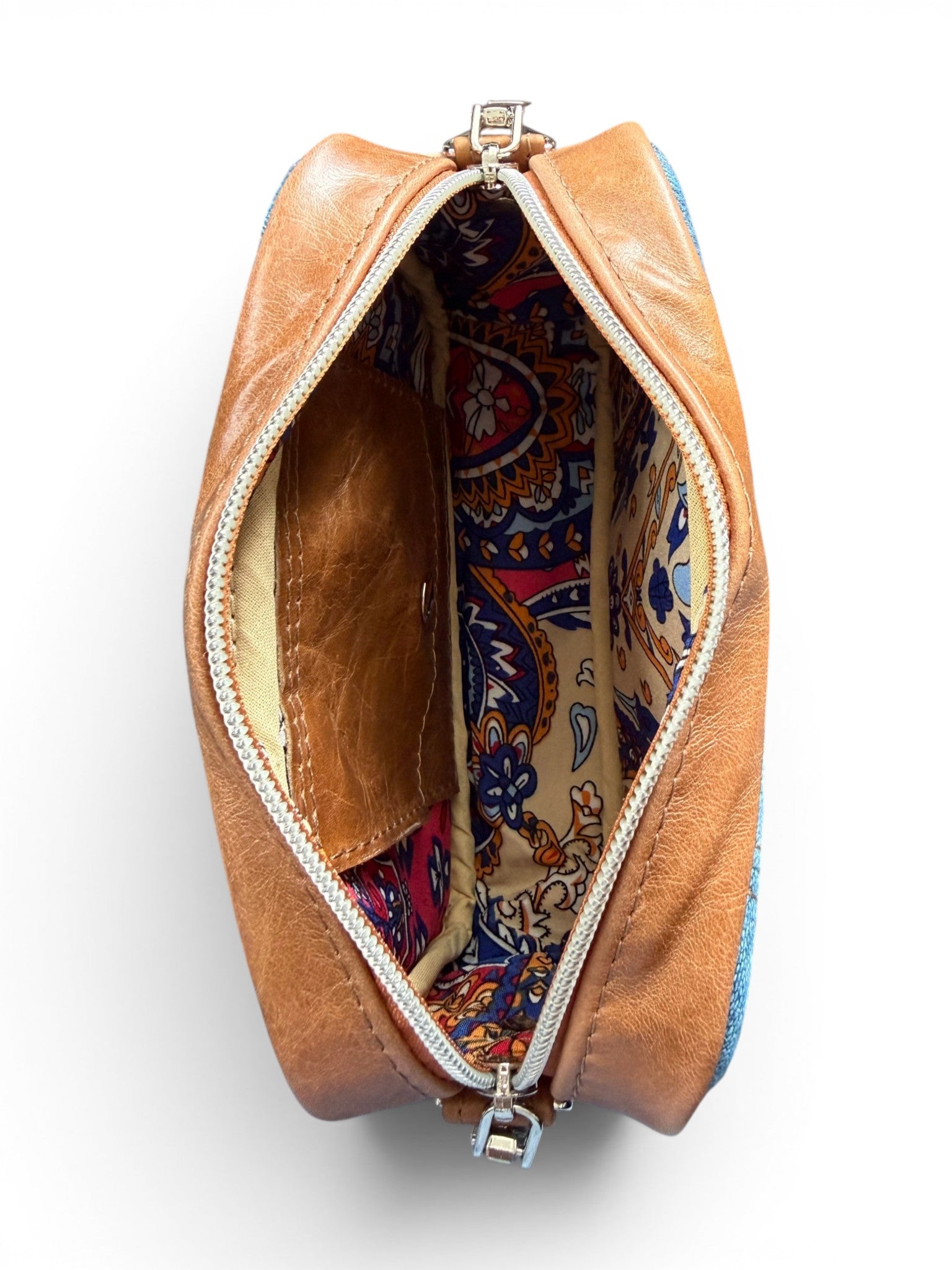 Birds eye view of a tan brown leather and denim bag, open to show the colorful interior lining on a white background