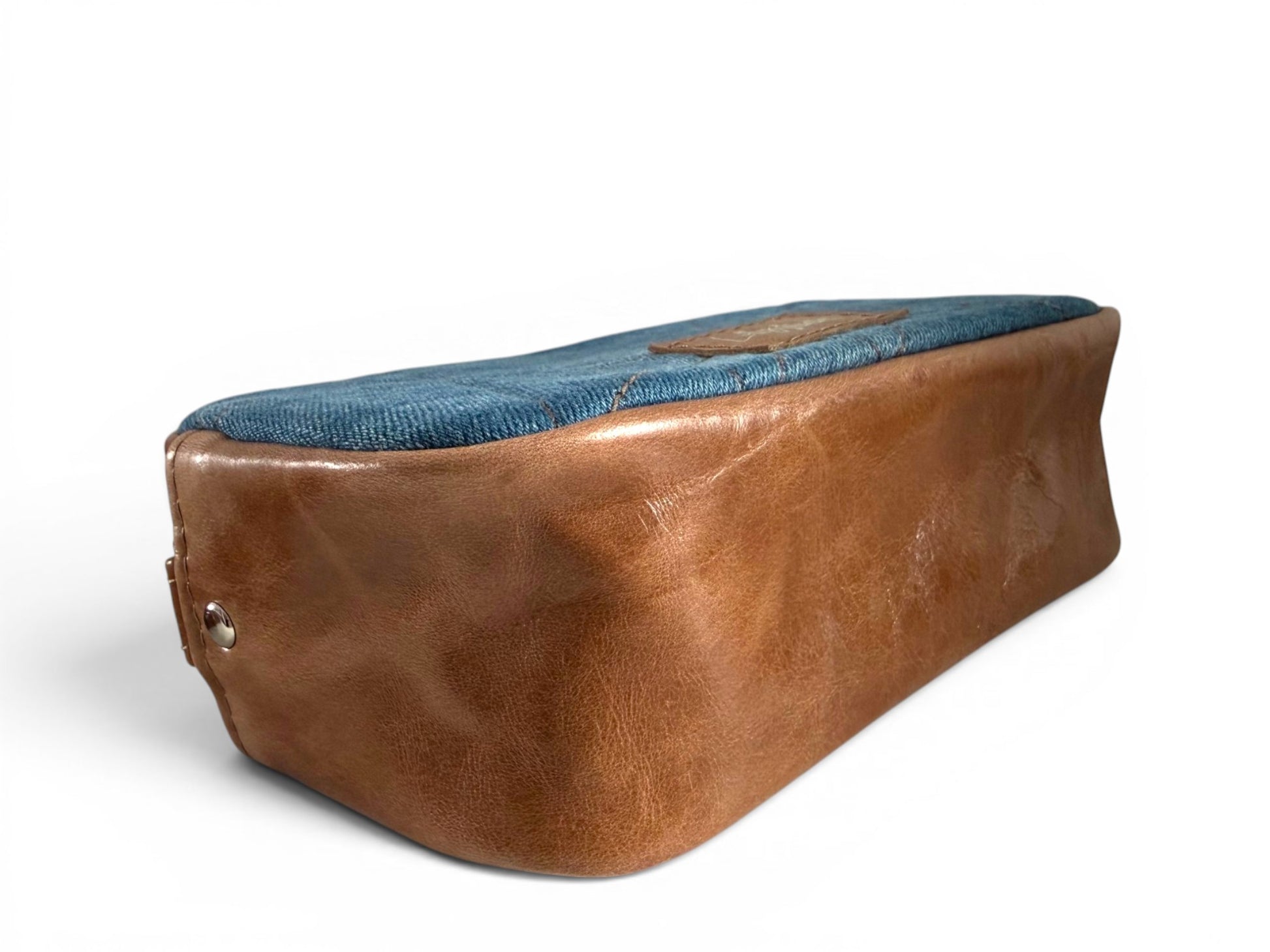 Bottom corner view of the Tiny Harriet compact crossbody bag, showing the tan leather gusset, sitting on a white background