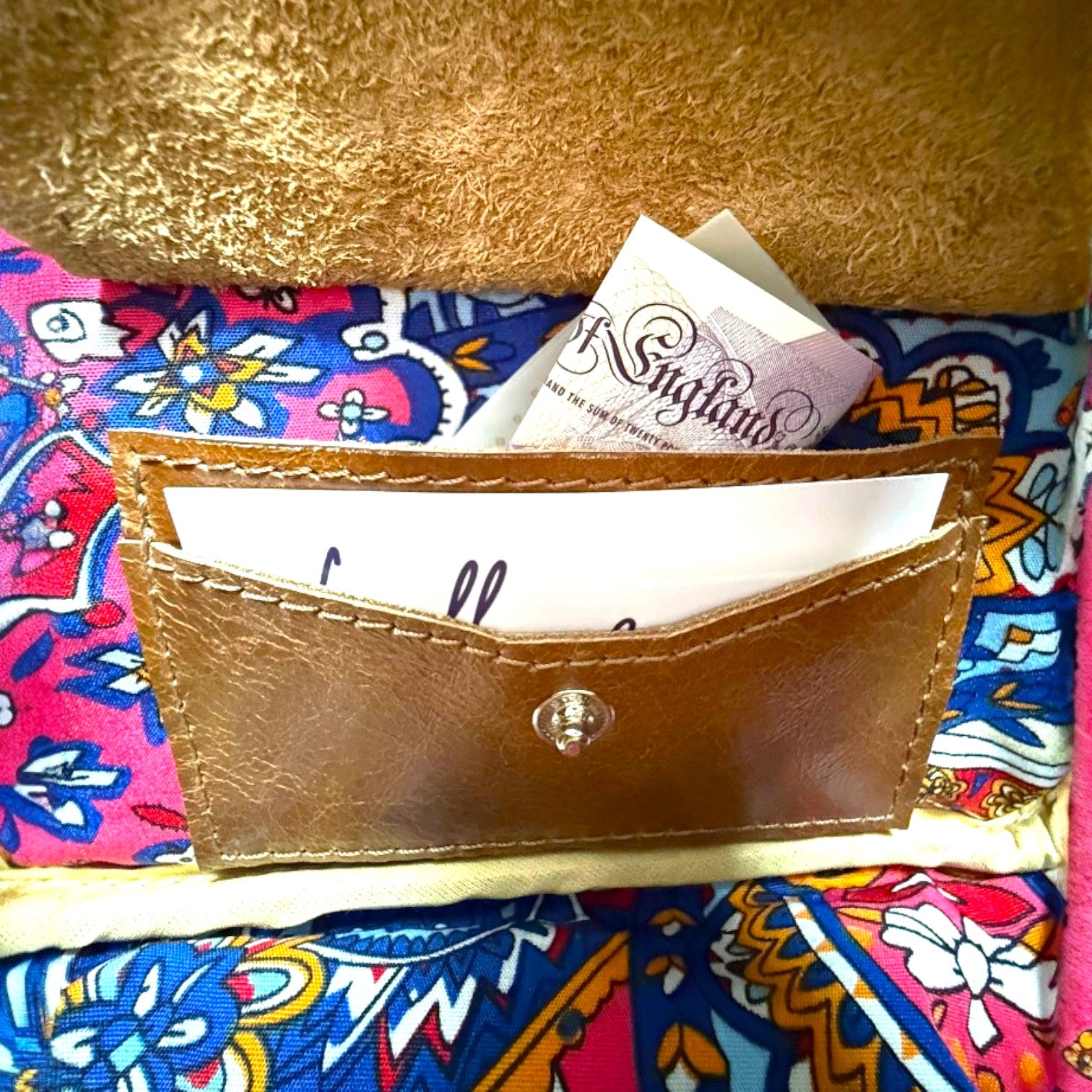 Brown leather cardholder with a button on a colorful fabric background