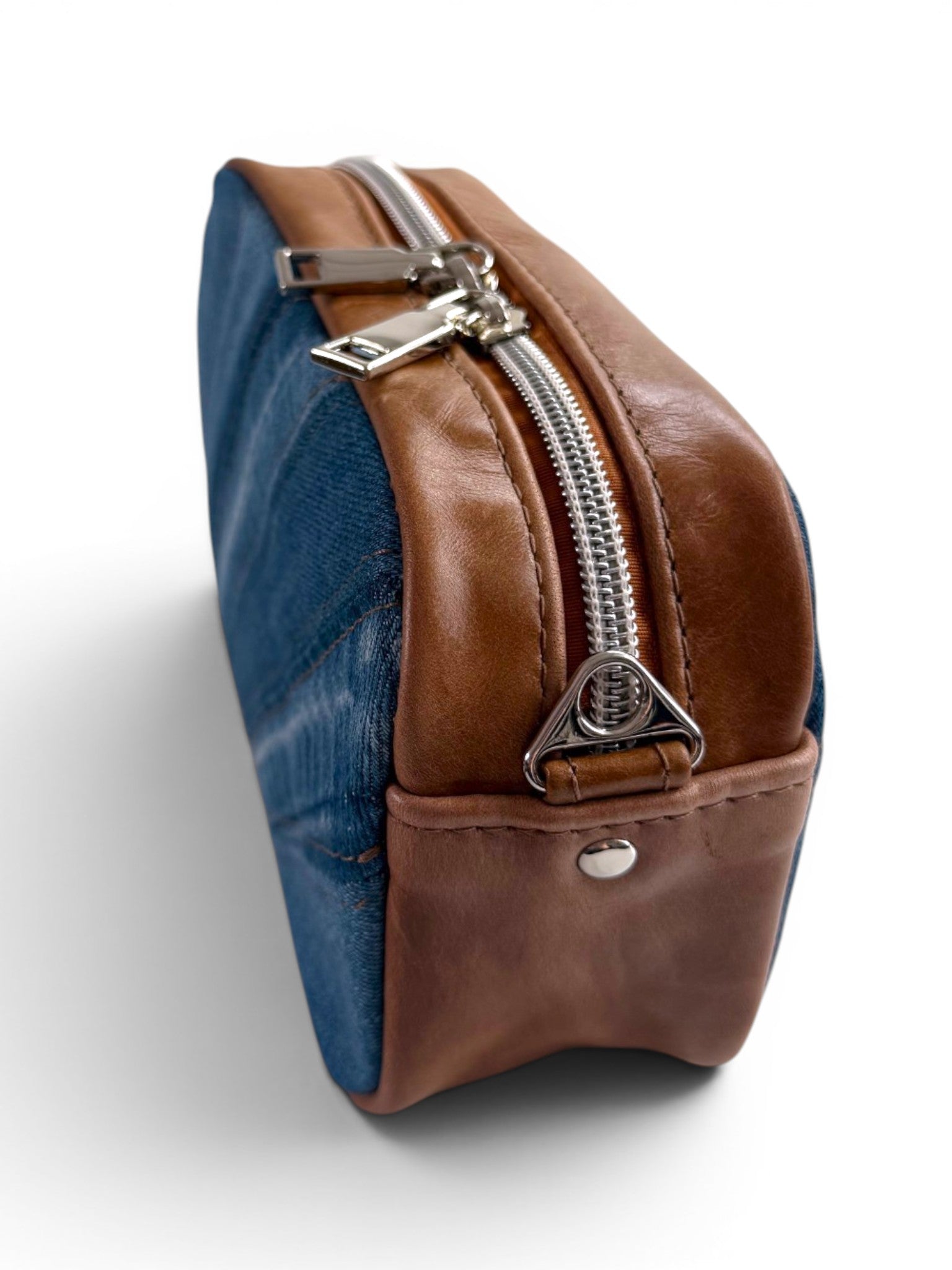 Side quarter view of a blue denim and tan coloured leather called the Tiny Harriet, compact crossbody bag. The image highlights the side, the zipper opening and the silver hardware.