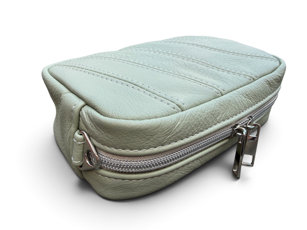 A light sage green pebbled leather zippered pouch with silver metal hardware, shown on a clean white background.