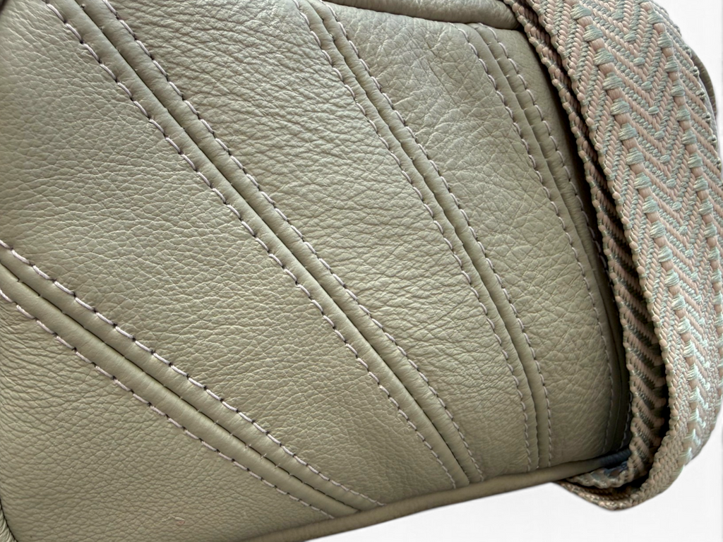 Close-up detail of a light sage green leather bag corner showing diagonal stitched panels and a woven strap in a matching beige and sage herringbone pattern.