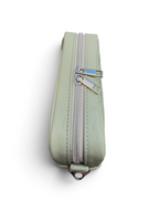 A sage green leather zippered compact crossbody bag with silver metal zippers and strap connectors, shown from a above on a white background.