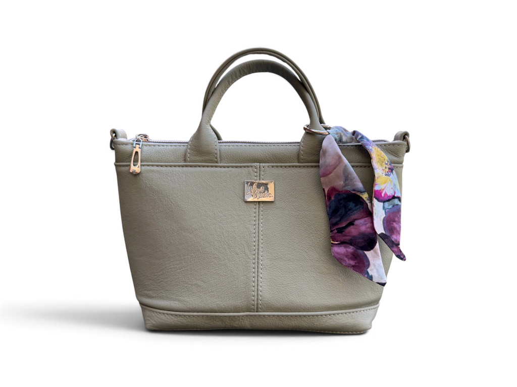 A structured light green grey leather handbag with dual top handles, a zipper top, and a small silver-tone logo plaque. A floral scarf in purple, pink, and blue is draped over the right side of the bag.