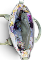 An open sage green handbag with a multicolour floral print lining, showing a zippered interior pocket and top handles against a white background.