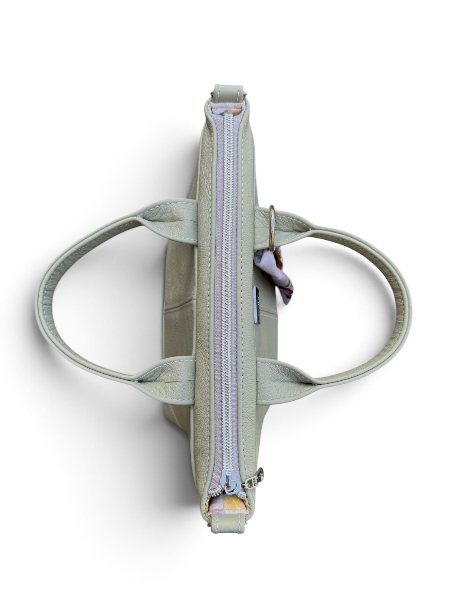 A sage green leather tote bag shown from a top-down view, featuring dual top handles, a central zippered compartment, and a small hanging keychain, set against a plain white background.