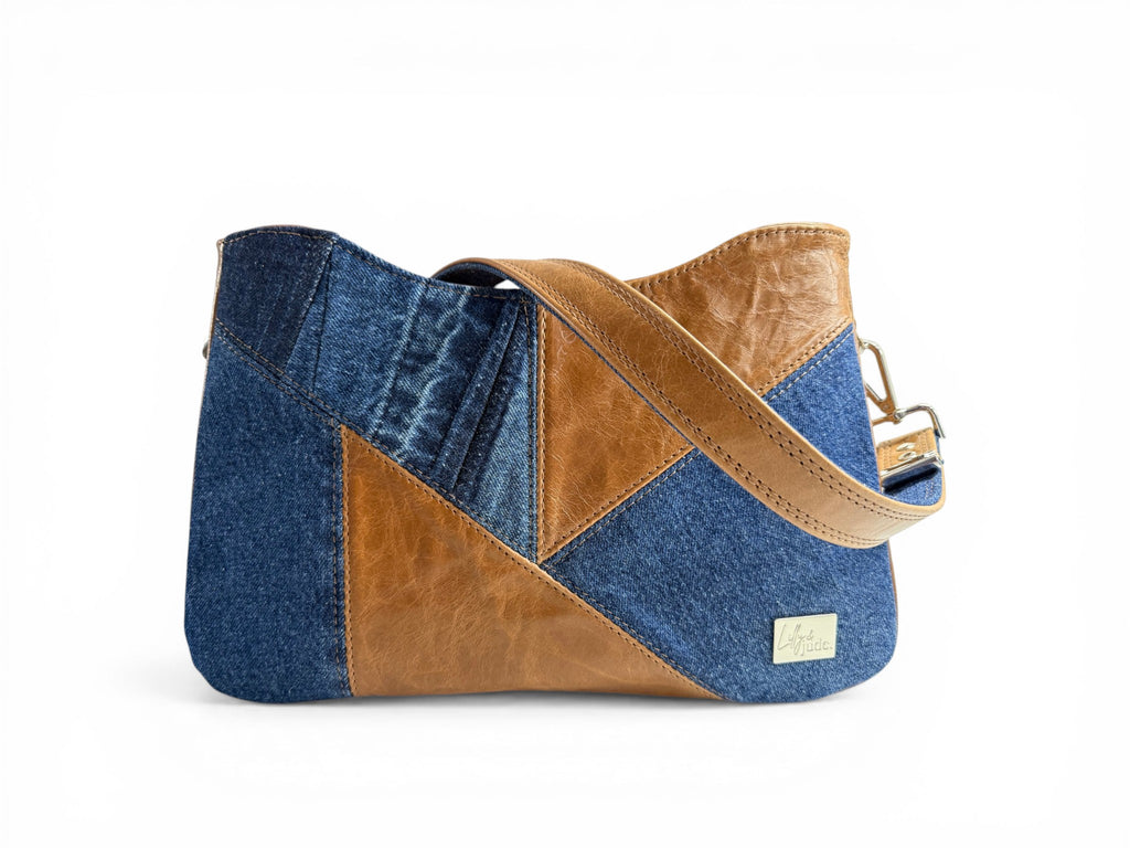 Upcycled demin and rescued tan coloured leather, patched handbag with shoulder strap wrapped over the top, sat on a white background