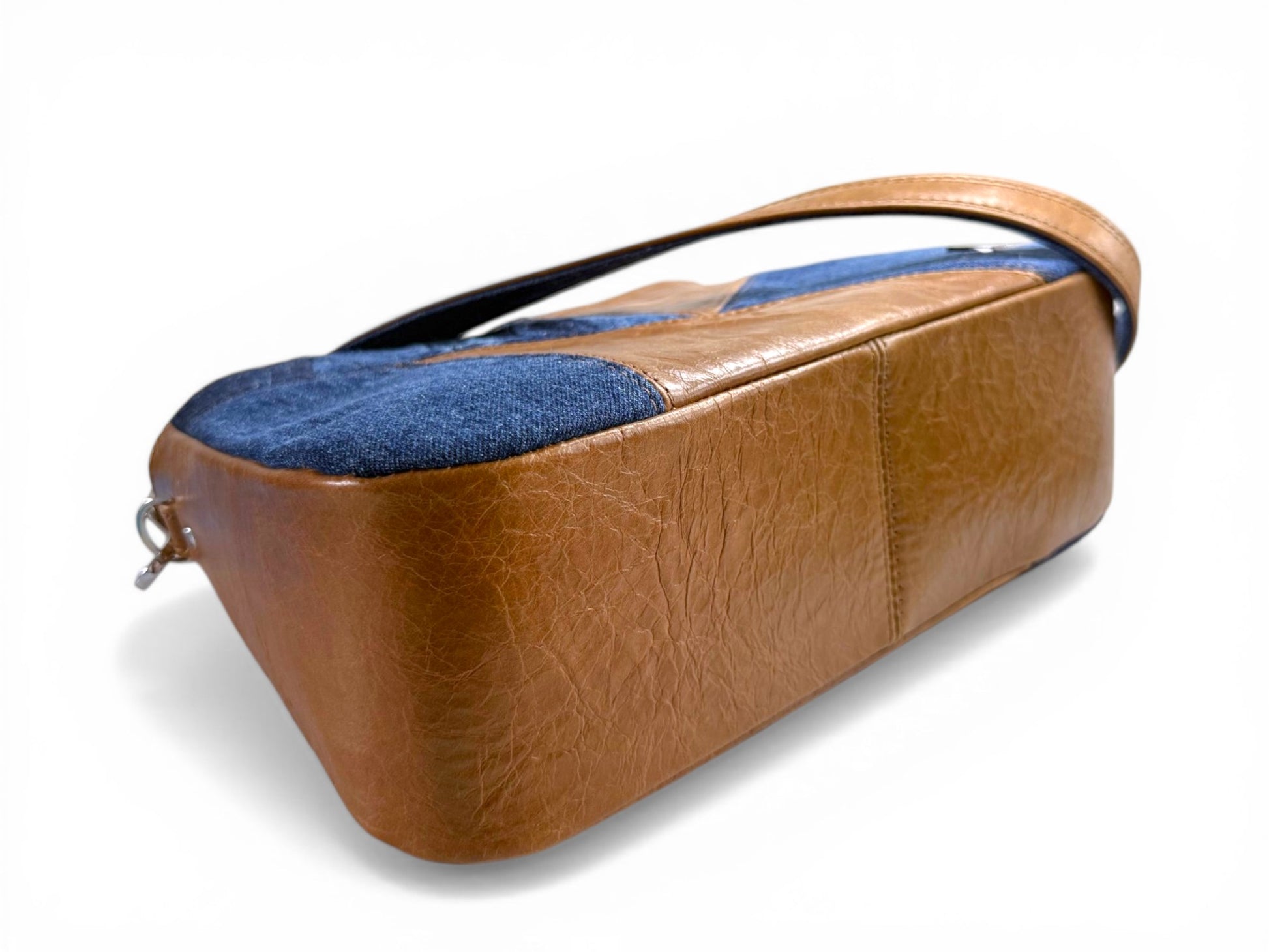 View of the bottom of the Veronica, a tan rown leather handbag with blue denim accents on a white background