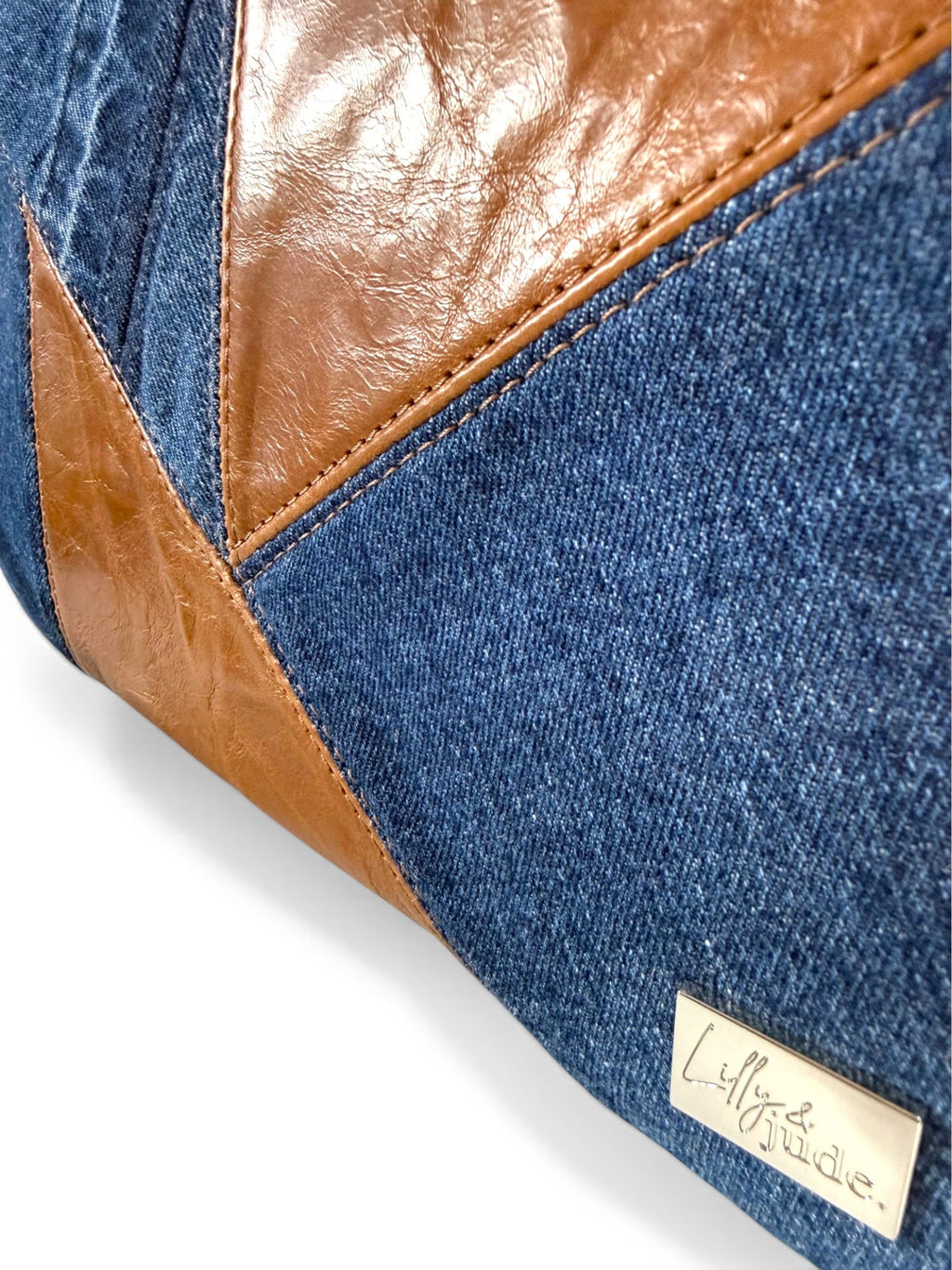 Close-up of a denim and brown leather bag with a silver Lilly & Jude brand label.