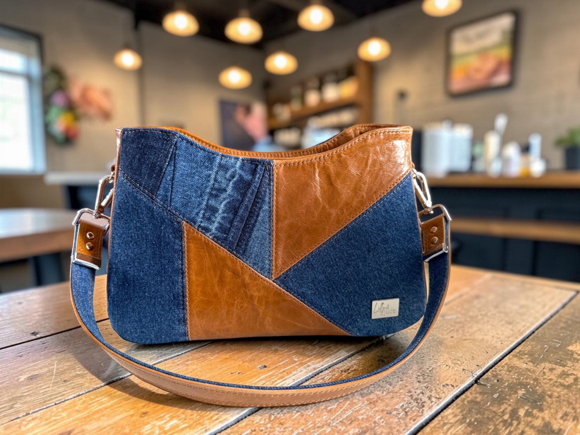 Denim and tan leather pieced handbag sat on a wooden table in a blurred, trendy bar