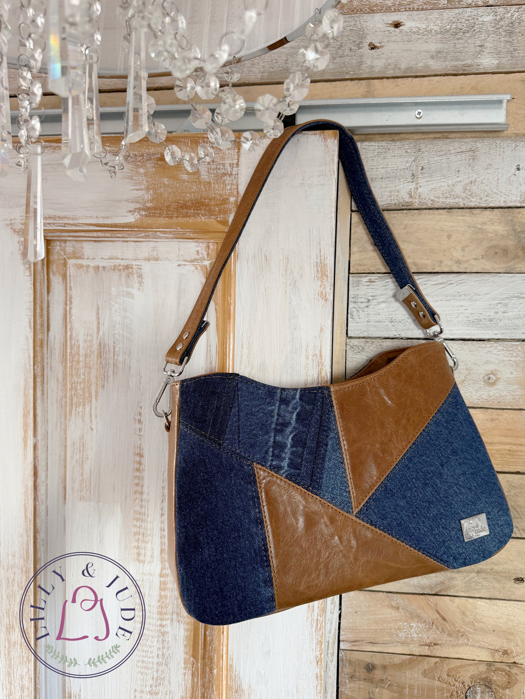 Image of Veronica, a tan leather and denim pieced, structured handbag hanging from the corner of a rustic style door