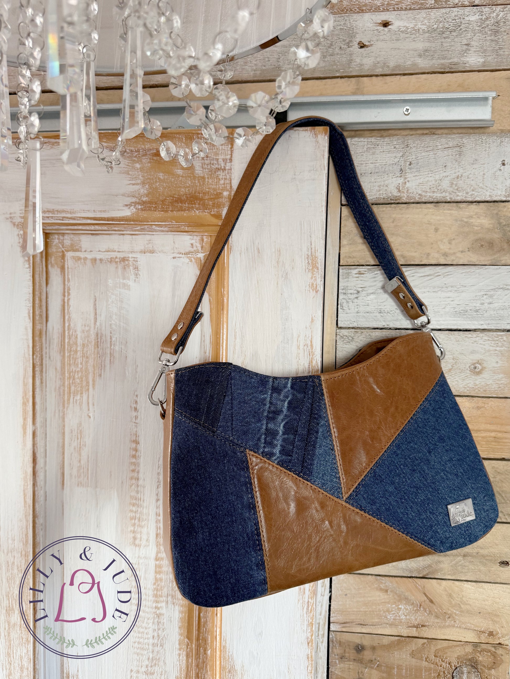 Image of Veronica, a tan leather and denim pieced, structured handbag hanging from the corner of a rustic style door