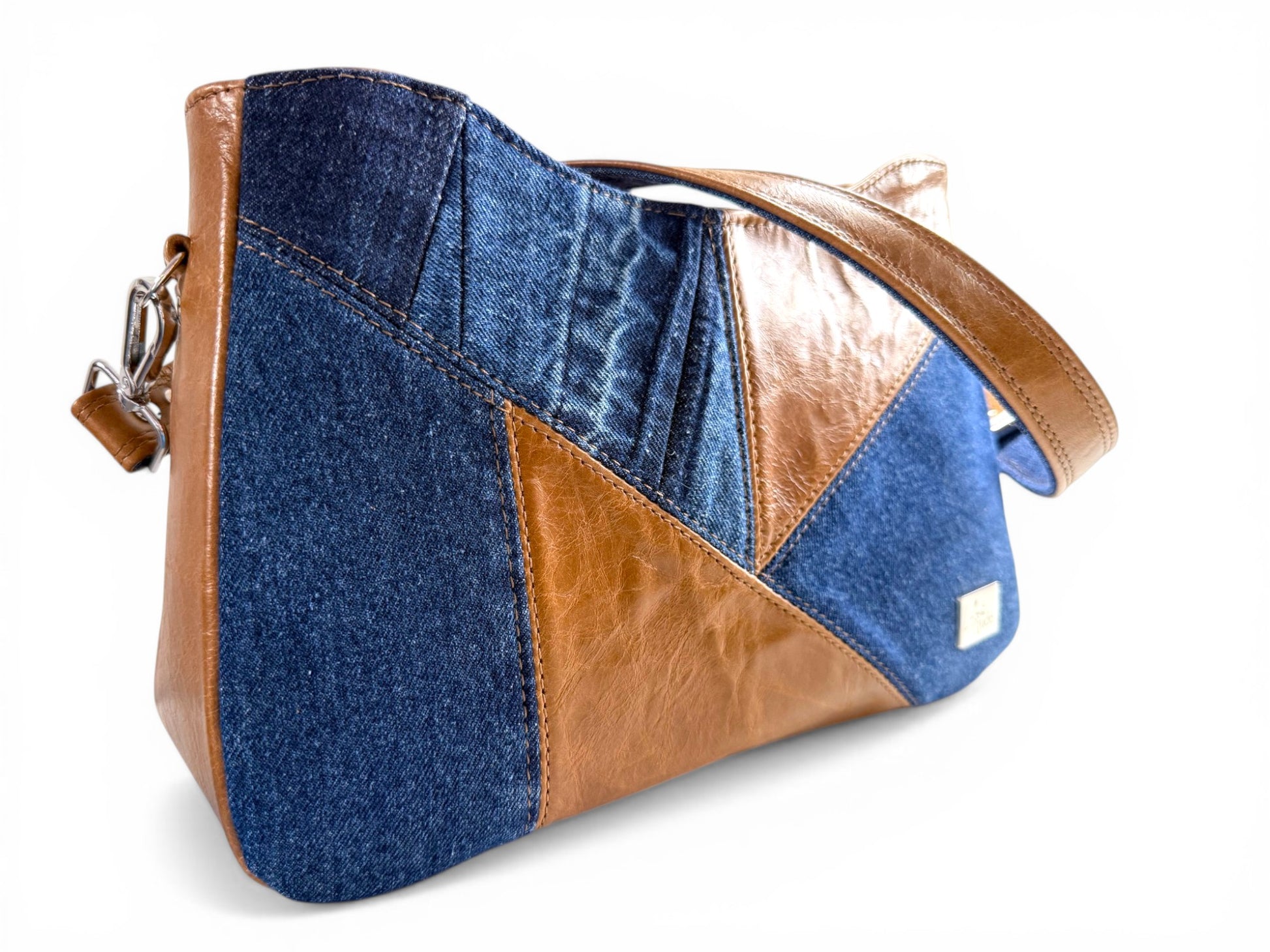 Stylish patchwork style handbag with blue denim and tan brown leather on a white background
