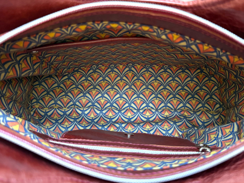 Top view of the Alaula leather shoulder bag with the zipper open showing Art Deco patterned lining and interior pockets.
