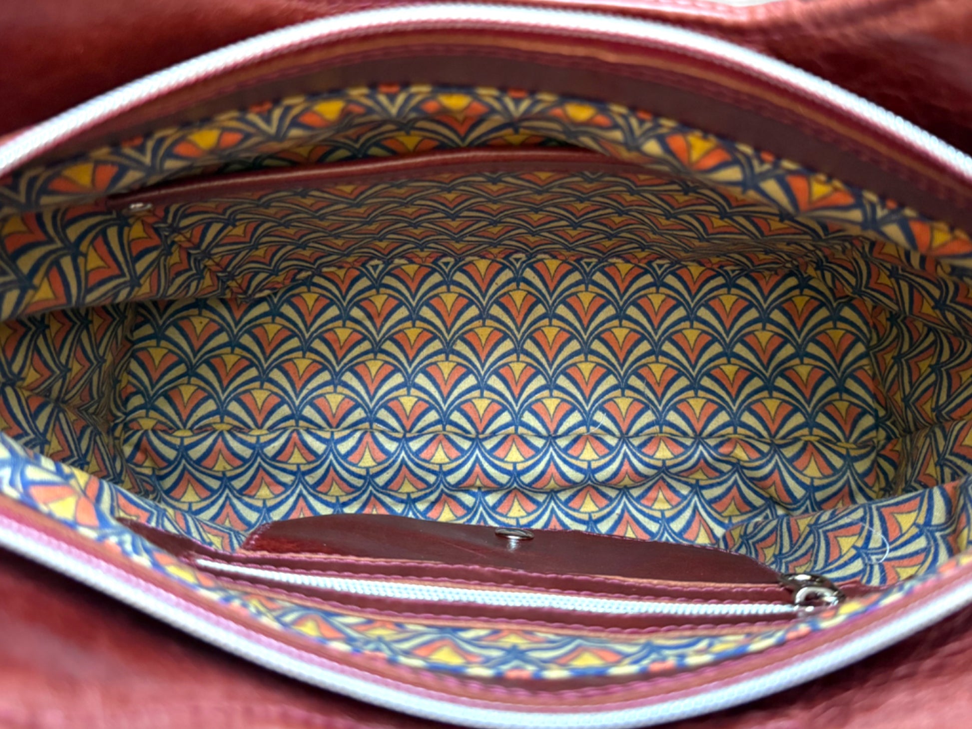Top view of the Alaula leather shoulder bag with the zipper open showing Art Deco patterned lining and interior pockets.
