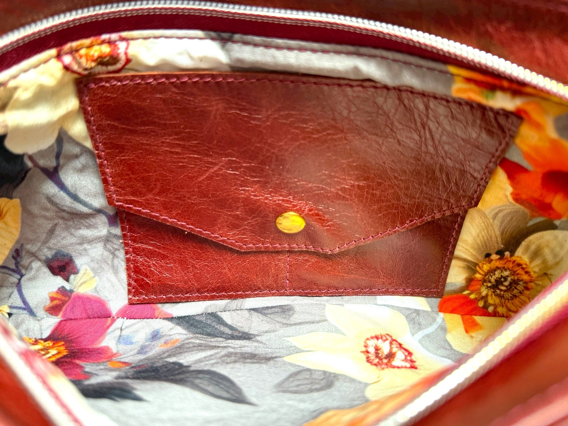 Closeup of the inside of the Betty Bow clutch bag. The image shows the grey and floral interior lining and the integrated purse, which is made from leather and has a gold press stud to keep your money secure