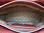 Top view of the Alaula leather shoulder bag with the zipper open showing Art Deco patterned lining and interior pockets.
